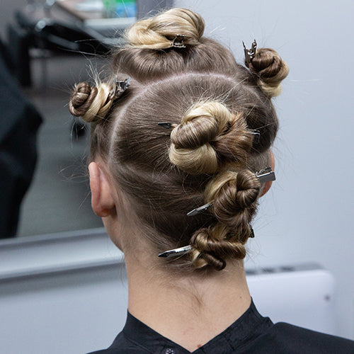 client's hair sectioned into multiple twisted buns secured with metal clips during the styling process.