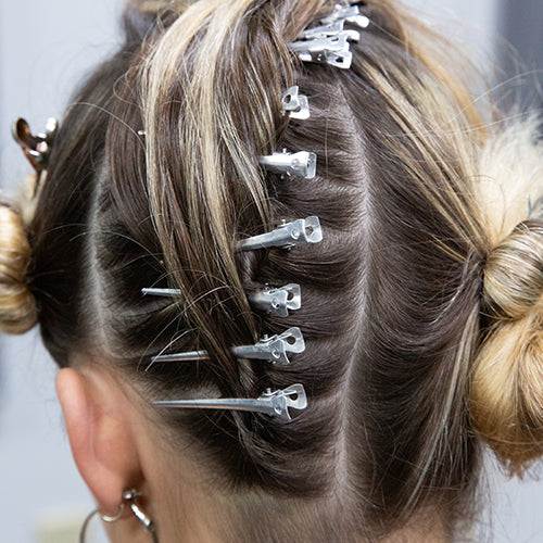 Close-up of a client's hair sectioned and clipped with metal hair clips during the styling process.