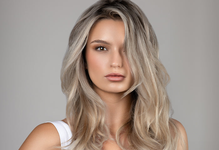 Portrait of a woman with styled, cool-toned blonde hair, wearing a white top against a light gray background.