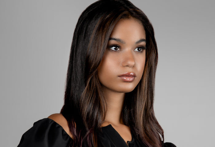 Portrait of a woman with sleek, dark brown hair featuring subtle highlights, wearing a black top against a light gray background.